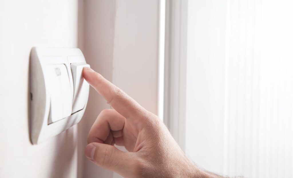 A person turns off a light switch to conserve energy.