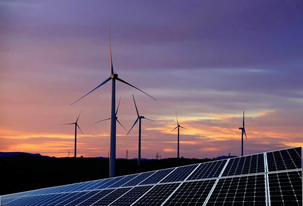 Solar panels with wind turbines at sunset.