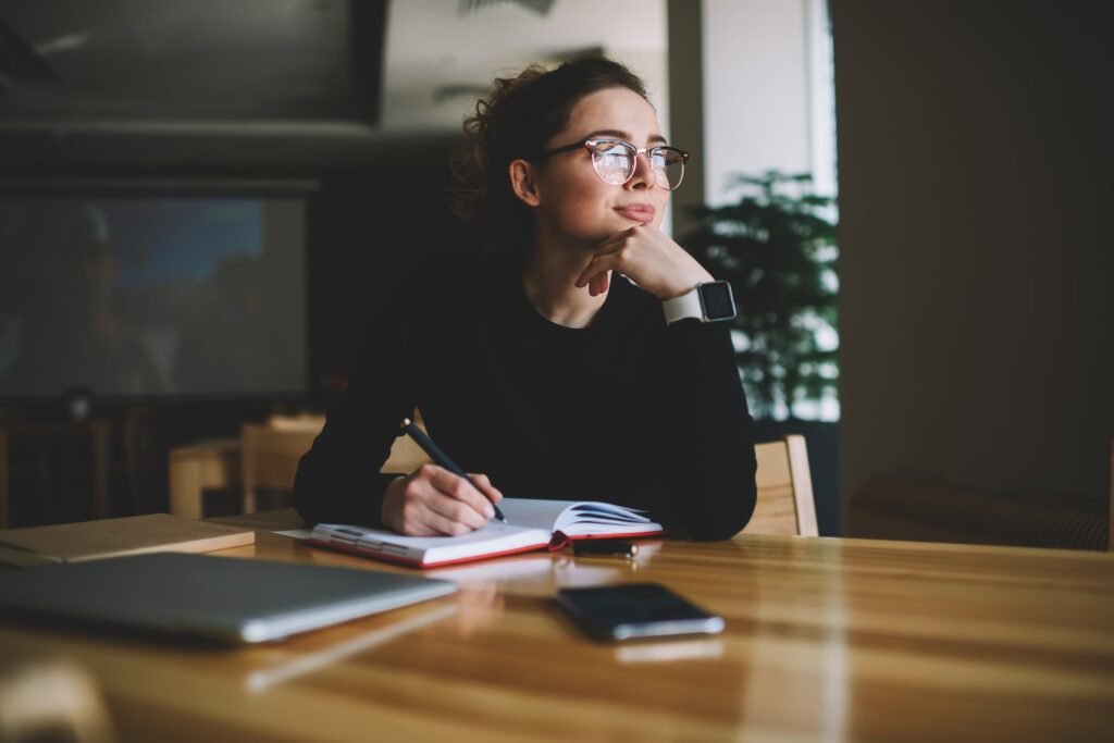 A young, female business owner thinks deeply while writing in a notebook