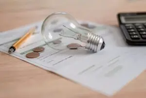 An energy bill on a table with a calculator, light bulb, pen and small change.