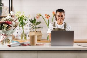 A small business owner works on her laptop in her floristry shop.